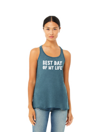 medium-skinned person with brown hair pulled back wearing a blue tank top with best day of my life written across in white block lettering.