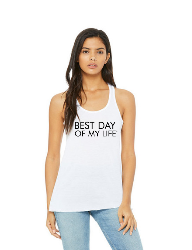 medium-skinned person with long brown hair wearing a white tank top with best day of my life written across in black.
