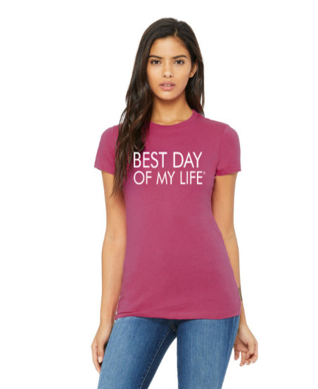medium-skinned person with long brown hair wearing a fitted dark pink crewneck t-shirt with best day of my life written across in white