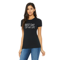medium-skinned person with long brown hair wearing a fitted black crewneck t-shirt with best day of my life written across in white