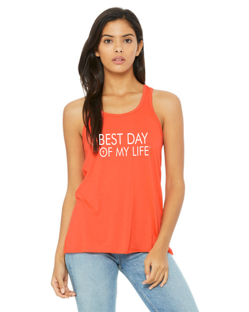 medium skinned person with long hair wearing an orange tank top with best day of my life written across in white and a cross in the O