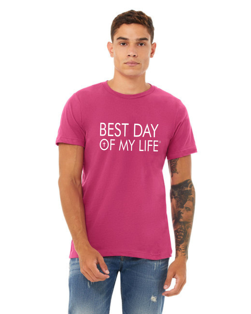medium skinned person with short brown hair wearing a bright pink crewneck t-shirt with best day of my life written in white with a cross in the O