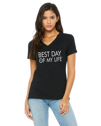 medium skinned person with long brown hair wearing a black vneck t-shirt with best day of my life written across in white with a cross in the O