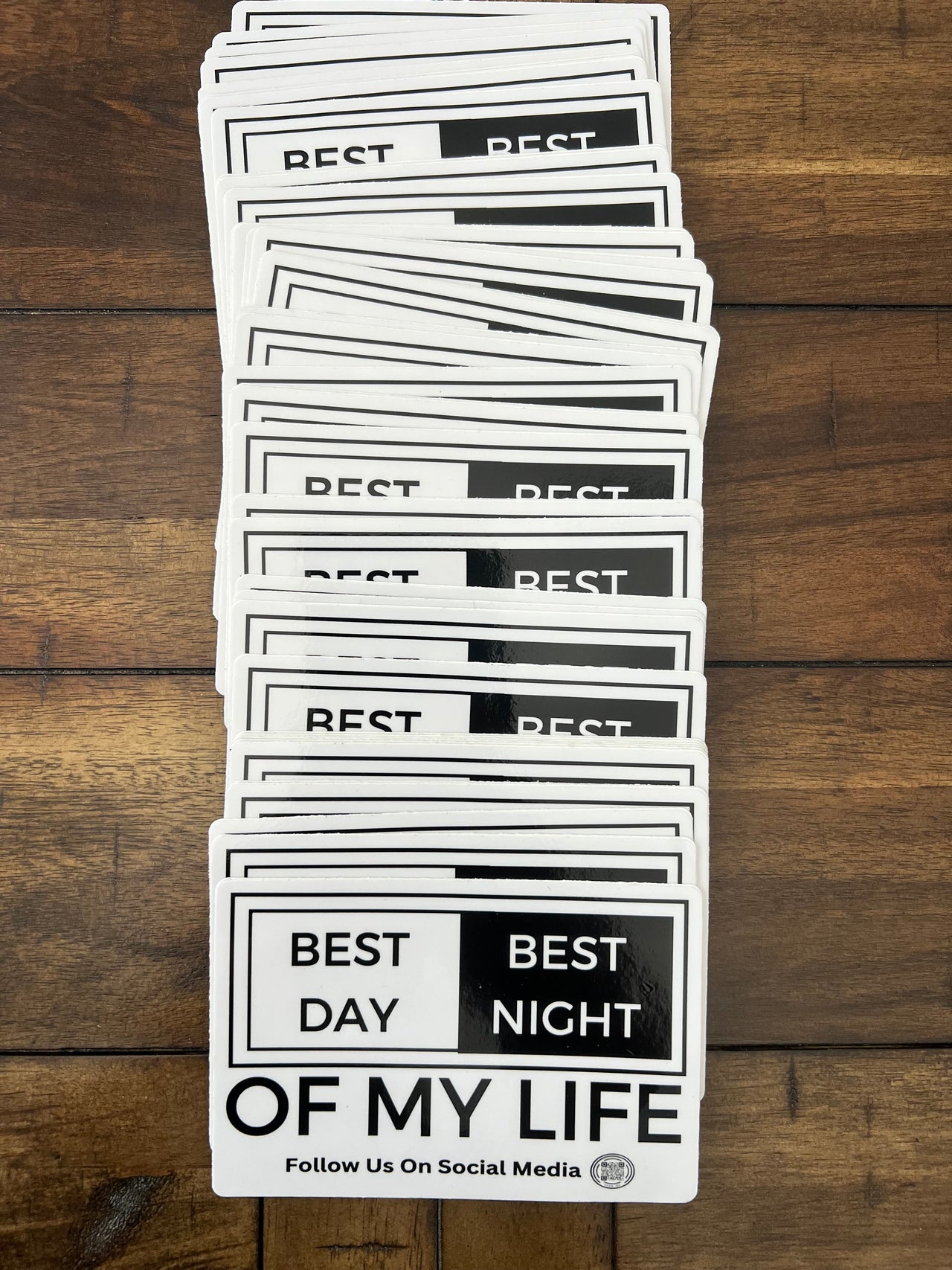 stack of stickers on wooden background, graphic of a white and black sticker on a grey background. sticker reads best day best night of my life