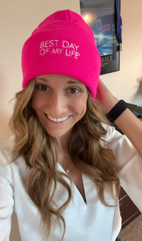 Thumbnail for white woman with blonde hair smiling and wearing bright pink beanie embroidered with best day of my life 